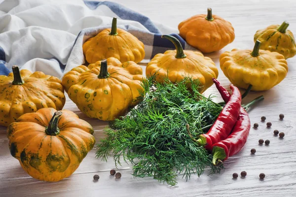 Yellow bush pumpkins, hot chilli peppers, dill bunch and whole dried allspice on white wooden table in the morning light. Ingredients for pickling