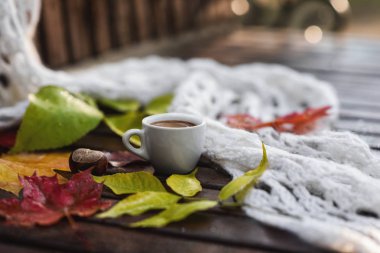 Sonbaharda ıslak ahşap tezgah üzerinde köpük, beyaz khitted şal, kuru renkli düşmüş yaprakları ve kestane ile kahve Seramik fincan. Close