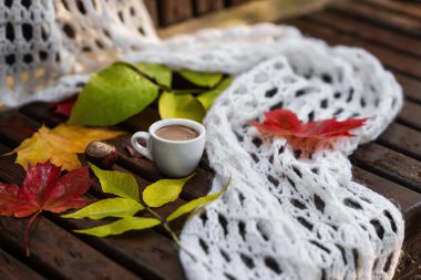 Seramik kahve fincanı, beyaz örme şal, sonbaharda yağmur damlaları ile ıslak ahşap tezgah üzerinde renkli düşmüş yaprakları ve kestane