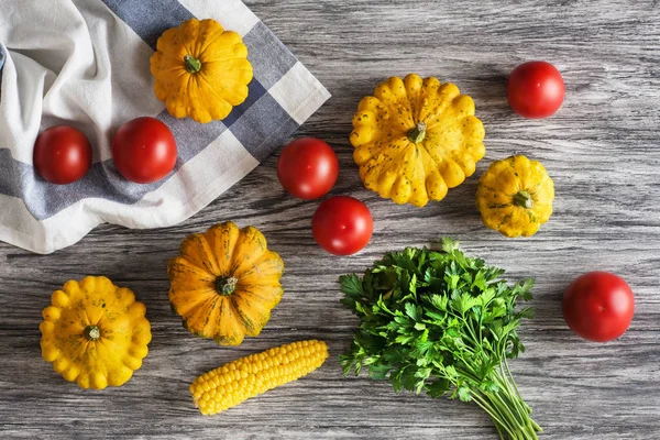 Vegetables: tomatoes, yellow bush pumpkins, corn and parsley bunch on gray wooden background. Healthy food and diet concept. Flat lay, top view