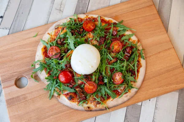 Kiraz domates, roka ve ahşap bir masa üzerinde burrata peynir ile ahşap bir gemide bir pizza havadan görünümü