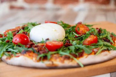 Kiraz domates, roka ve arka plan için ahşap bir masa ve tuğla duvar burrata peynir ile ahşap bir gemide bir pizza yan görünüm