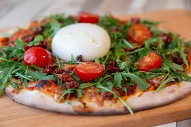 Kiraz domates, roka ve arka plan için ahşap bir masa ve tuğla duvar burrata peynir ile ahşap bir gemide bir pizza yan görünüm