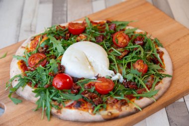 Kiraz domates, roka ve arka plan için ahşap bir masa ve tuğla duvar burrata krem peynir ile ahşap bir gemide pizza