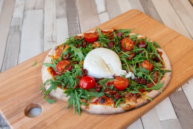 Kiraz domates, roka ve arka plan için ahşap bir masa ve tuğla duvar burrata krem peynir ile ahşap bir gemide pizza
