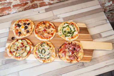 Bir tuğla duvar ile ahşap bir masa üzerinde bir ahşap tahta üzerinde altı farklı pizza havadan görünümü