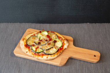Bir pizza ile kabak, patlıcan ve kuru domates graten mozzarella peyniri ile hava görünümünü. Bir ahşap tahta ve gri masa örtüsü