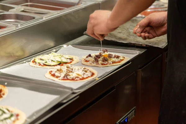 Close up of chef hands adding ingredients like and egg on a pizza on a restaurant kitchen in a metallic tray
