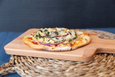 Rafya daire mavi masa örtüsü yemeye hazır ile ahşap bir gemide pesto pizza mor soğan ile yan görünüm