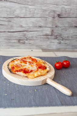 Küçük margarita pizza domates ve peynirli bir gri masa örtüsü ve ahşap bir daire ahşap panosunda, kiraz domates ile garnitür