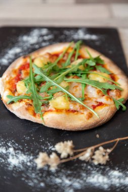 Bir pizza roka, peynir ve domates un ile bir yazı tahtası garnitür olarak ve bir tuğla duvar ile ahşap bir masaya kuru çiçek ile yakın çekim.