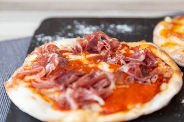 jambon pizza yakın çekim üzerinde un bir ahşap beyaz tabloda gri bir masa örtüsü ile bir kara tahta garnitür