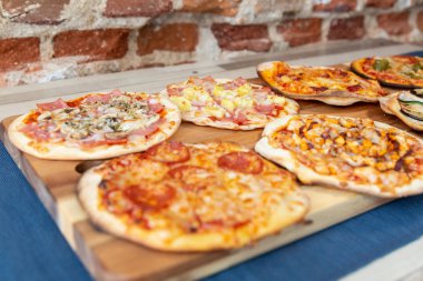 Yedi küçük pizza fırın dışında taze bir ahşap tahtada bir restoran yemek hazır. Carbonara ve hawaiian olanlar üzerinde odaklanmıştır. Ahşap bir masaya mavi bir masa örtüsü ve bir tuğla duvar