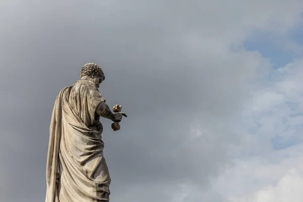 an ancient stone statue of a man holding a key in the blue sky in Rome, Italy