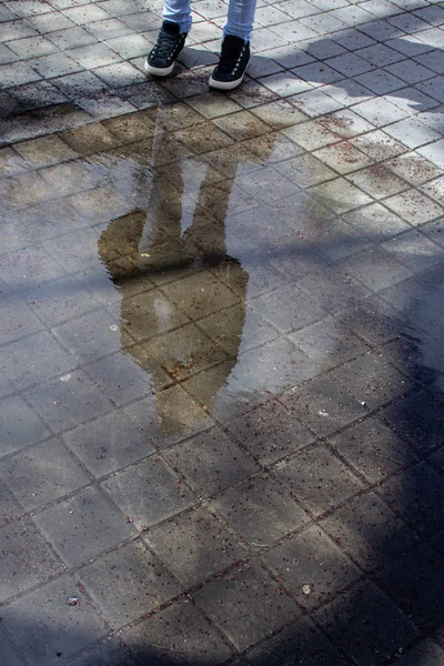 reflection of a young woman on a puddle in the street with black sneakers and jeans