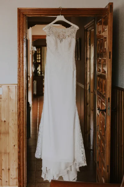a white wedding dress hanging on a wooden door in a rustic house