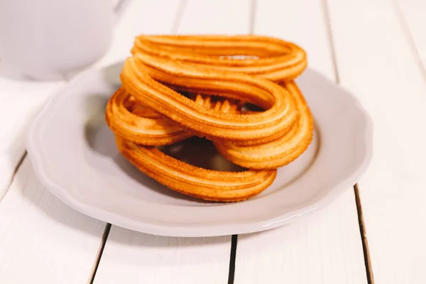 Beignets espagnols servis sur un plat blanc sur une table en bois avec une tasse de chocolat chaud — Photo