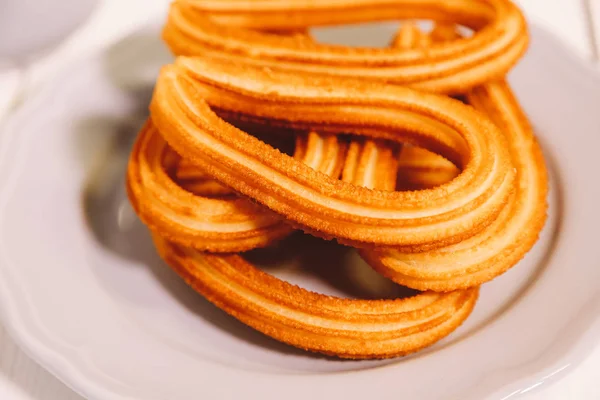 Gorengan Spanyol disajikan pada piring putih di atas meja kayu dengan secangkir cokelat panas — Stok Foto