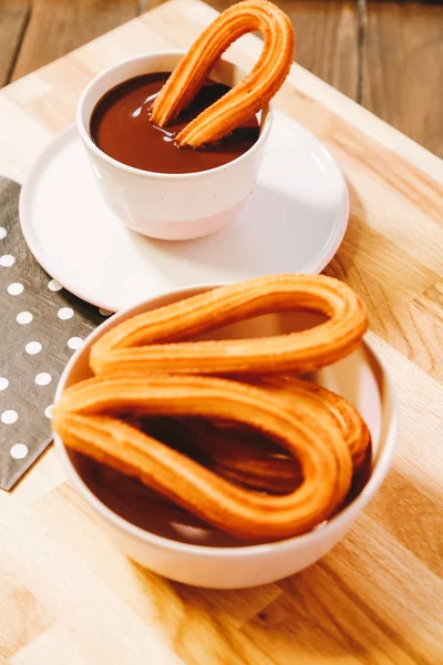 Buñuelos españoles servidos en una mesa de madera con una taza de chocolate caliente — Foto de Stock