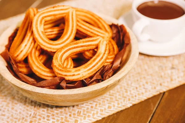 Gorengan Spanyol disajikan di atas meja kayu dengan secangkir cokelat panas — Stok Foto