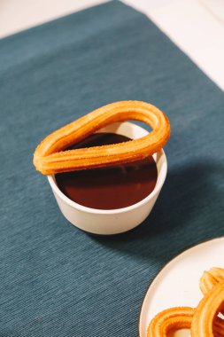 İspanyol börek bir fincan sıcak çikolata ve mavi masa örtüsü üzerinde hizmet