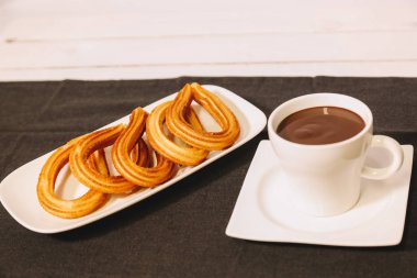 İspanyol börek gri masa örtüsü ve sıcak çikolata bir fincan ile ahşap bir masada hizmet