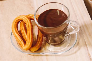 sıcak çikolata ve iki İspanyol börek ile bir cam fincan ahşap tahta üzerinde hizmet