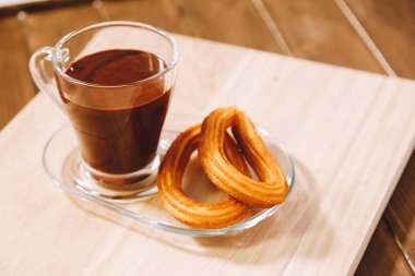 sıcak çikolata ve iki İspanyol börek ile bir cam fincan ahşap tahta üzerinde hizmet