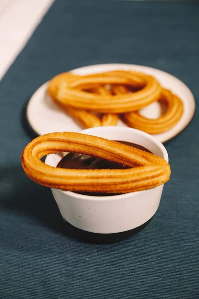 Buñuelos españoles servidos sobre una mesa de madera y un mantel azul con una taza de chocolate caliente — Foto de Stock