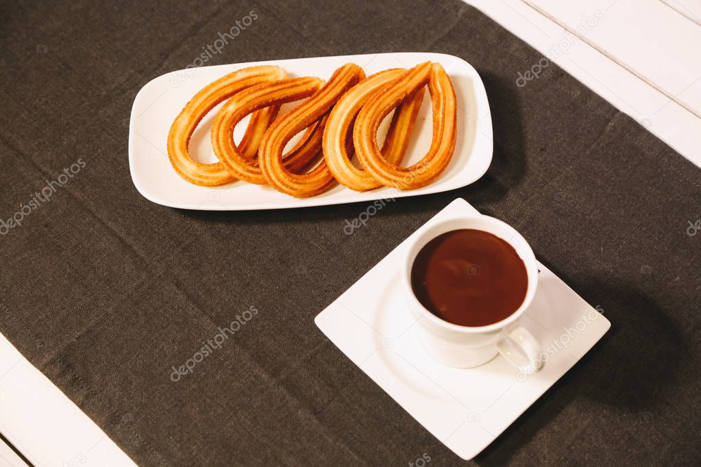 spanish fritters served on a wooden table with a gray tablecloth and a cup of hot chocolate