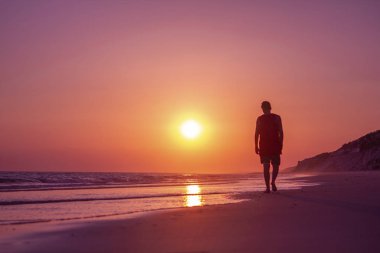 Adam gün batımında sahilde yürüyor.