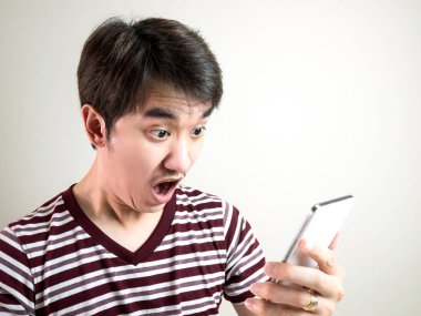 Smartphone arıyorsunuz ve duygu Genç Asyalı adam şok ve gri arka plan ile şaşırttı.