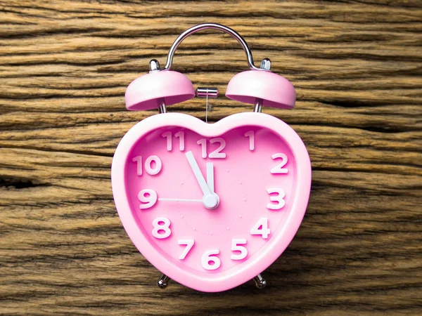 Pink alarm clock in the form of heart on wooden background.