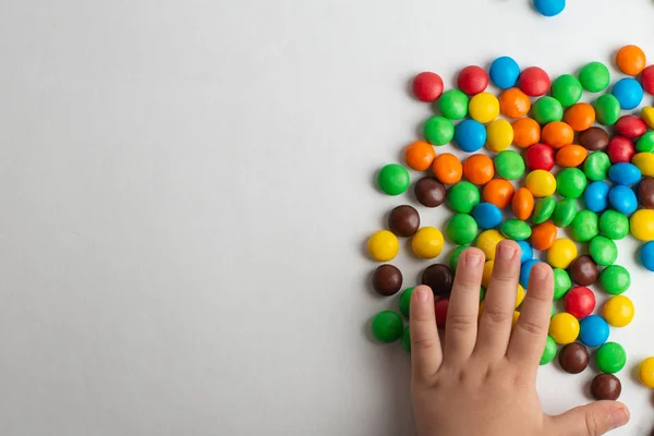 Doces de chocolate coloridos no fundo branco com mão de criança — Fotografia de Stock