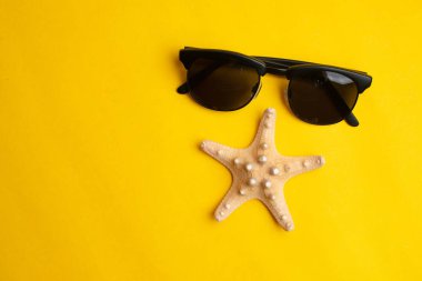 Sarı backgrou üzerinde yaz aksesuarları, deniz kabuğu ve güneş gözlüğü