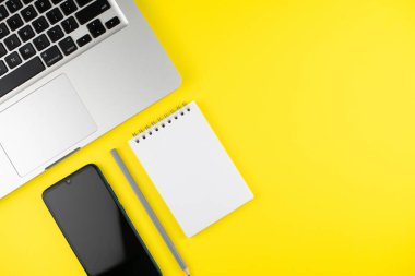 Sarı arka planda not defteri, kalem, telefon ve laptop. Kopyalama alanı olan üst görünüm. Ofisteki işyerinde. Düz yatıyordu. Model.