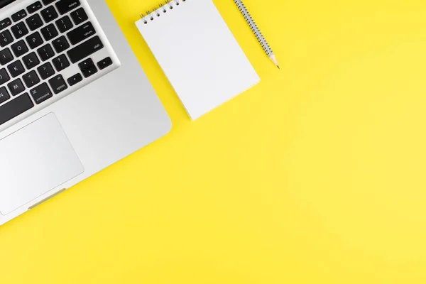 Not defteri, kalem ve dizüstü bilgisayar sarı arka planda. Kopyalama alanı olan üst görünüm. Ofisteki işyerinde. Düz yatıyordu. Model.
