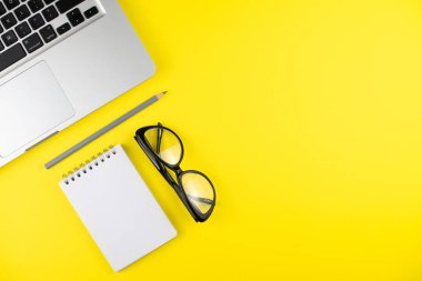 Laptop, mor gözlük, kalem, sarı arka planda not defteri planlayıcısı. Düz yatıyordu. Uzayı kopyala Ofiste işyeri. 