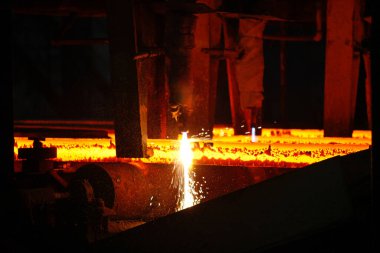 Meşalenin yanındaki çelik bölmeler metalürjik bitkileri kesiyor. Metalurjik üretim, ağır sanayi, mühendislik, çelik yapımı. 