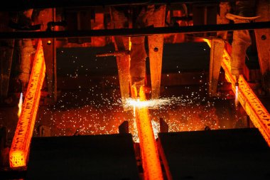 Meşalenin yanındaki çelik bölmeler metalürjik bitkileri kesiyor. Metalurjik üretim, ağır sanayi, mühendislik, çelik yapımı