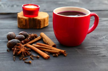 Noel ahşap arka plan üzerinde kırmızı mug içinde baharatlar ile şarap mulled. Tarçın, Hindistan cevizi, Yıldız anason, karanfil.
