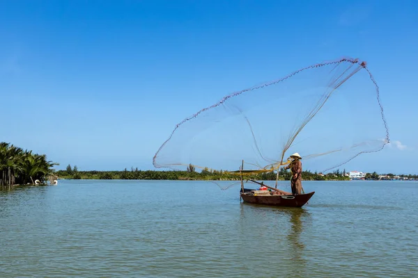 A traditional fisherman is throwing a fishing net at Hoi An in Vietnam