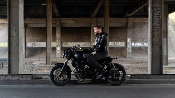 Cara em uma motocicleta preta ficar sob a ponte — Fotografia de Stock