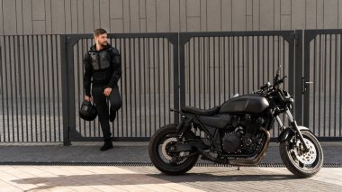 Yakışıklı olan binici bir sakal ve bıyık standları çit duvar near. Bisiklet sipariş vintage bir garajda. Acımasız kentsel yaşam tarzı