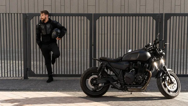 Handsome guy rider with a beard and mustache, stands near the wall of the fence. Bicycle to order in a vintage garage. Brutal urban lifestyle