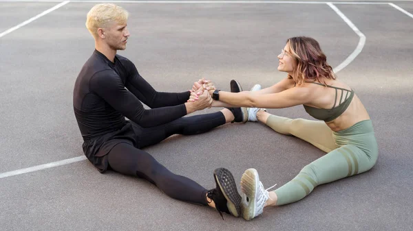 Athletic woman and man sitting on the sports field and holding hands — Stock Photo, Image