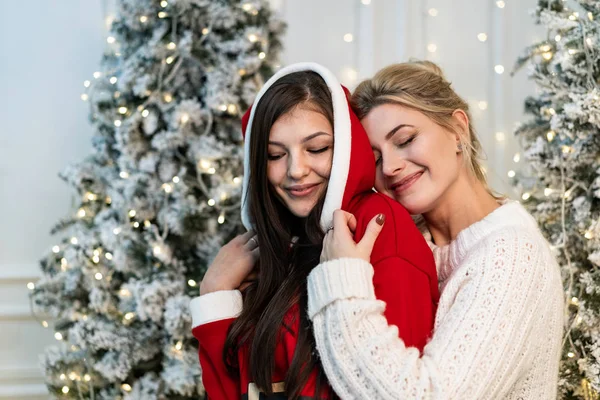 Duas irmãs bonitas em suéteres abraçando perto da árvore de Natal — Fotografia de Stock