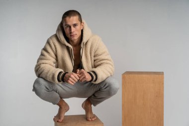Ahşap küp ve poz eşofman akıllı ciddi genç adam çömelmiş