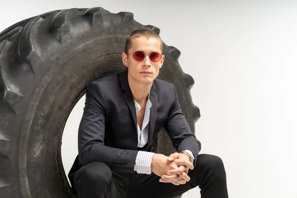 Elegante hombre guapo en traje negro sentado en el neumático — Foto de Stock