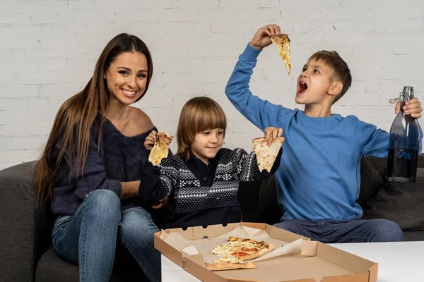 Vacker ung brunet mamma med lite söner poserar tillsammans med pizza — Stockfoto